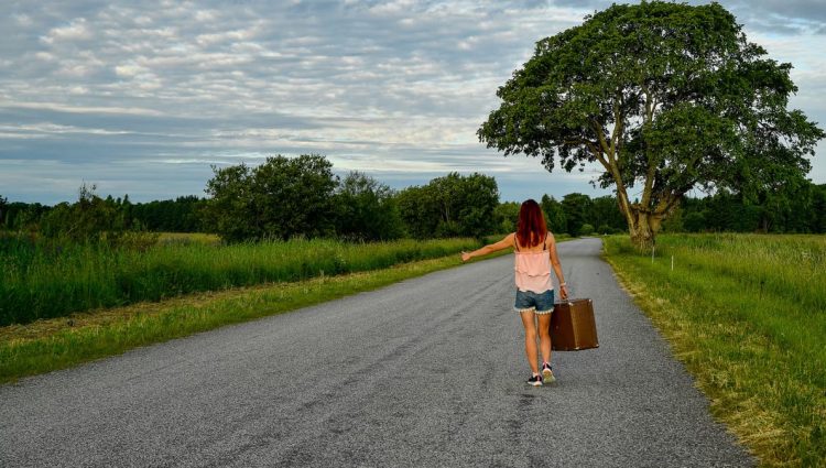 A woman with red hair hitchhiking in the Estonian countryside on a sunny summer day.